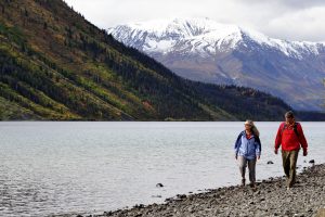 Two people hiking beside a river and mountain range in the Yukon.