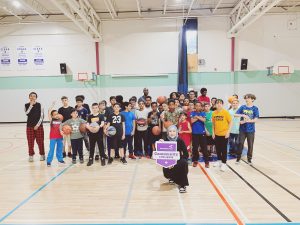 A woman kneeling in front of a group of kids while holding up a ParticipACTION Community Challenge sign in a school gymnasium.