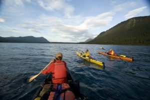 A group of people canoeing and kayaking on a lake surrounded by mountains in the Yukon.