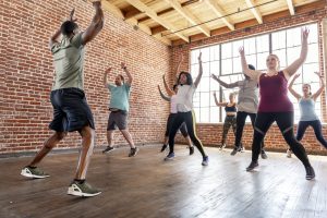 A group of people doing jumping jacks in an exercise studio.