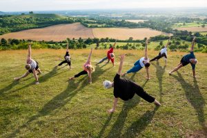 A group of people doing yoga on a grassy hill.